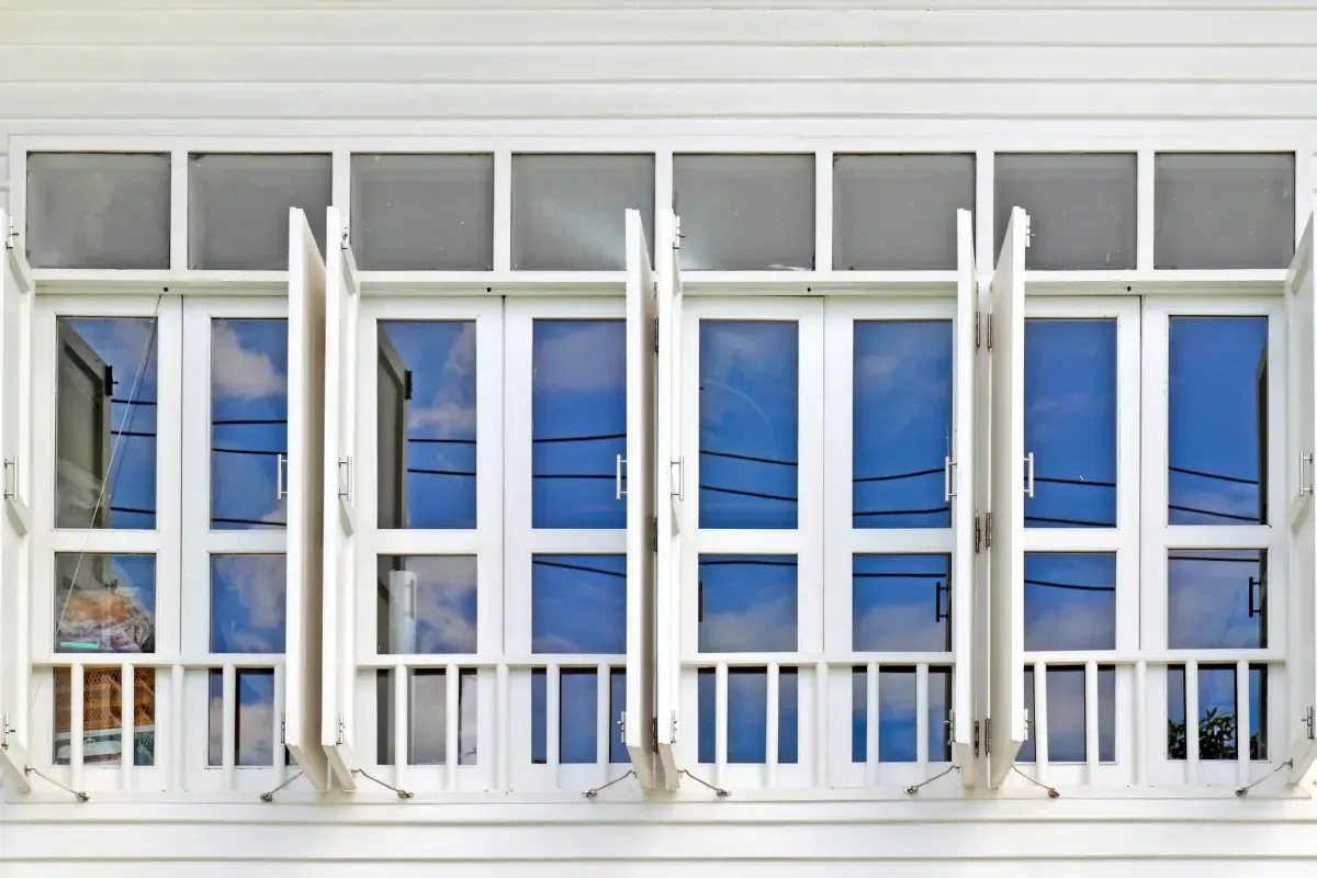 Un conjunto de ventanas blancas de varios paneles con contraventanas abiertas, que reflejan un cielo azul