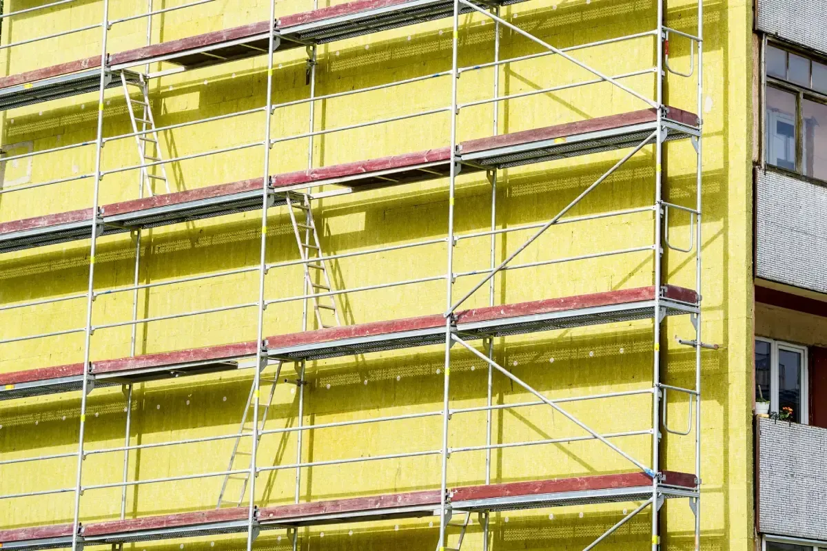 La fachada de un edificio está cubierta con paneles de aislamiento térmico amarillos, enmarcada por andamios metálicos
