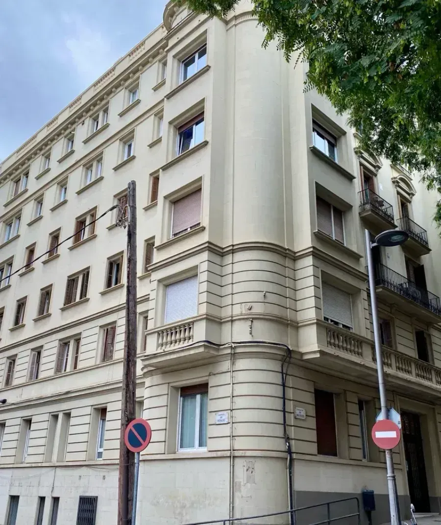 Un edificio de apartamentos de varias plantas, de color beige, situado en una esquina, con ventanas rectangulares.