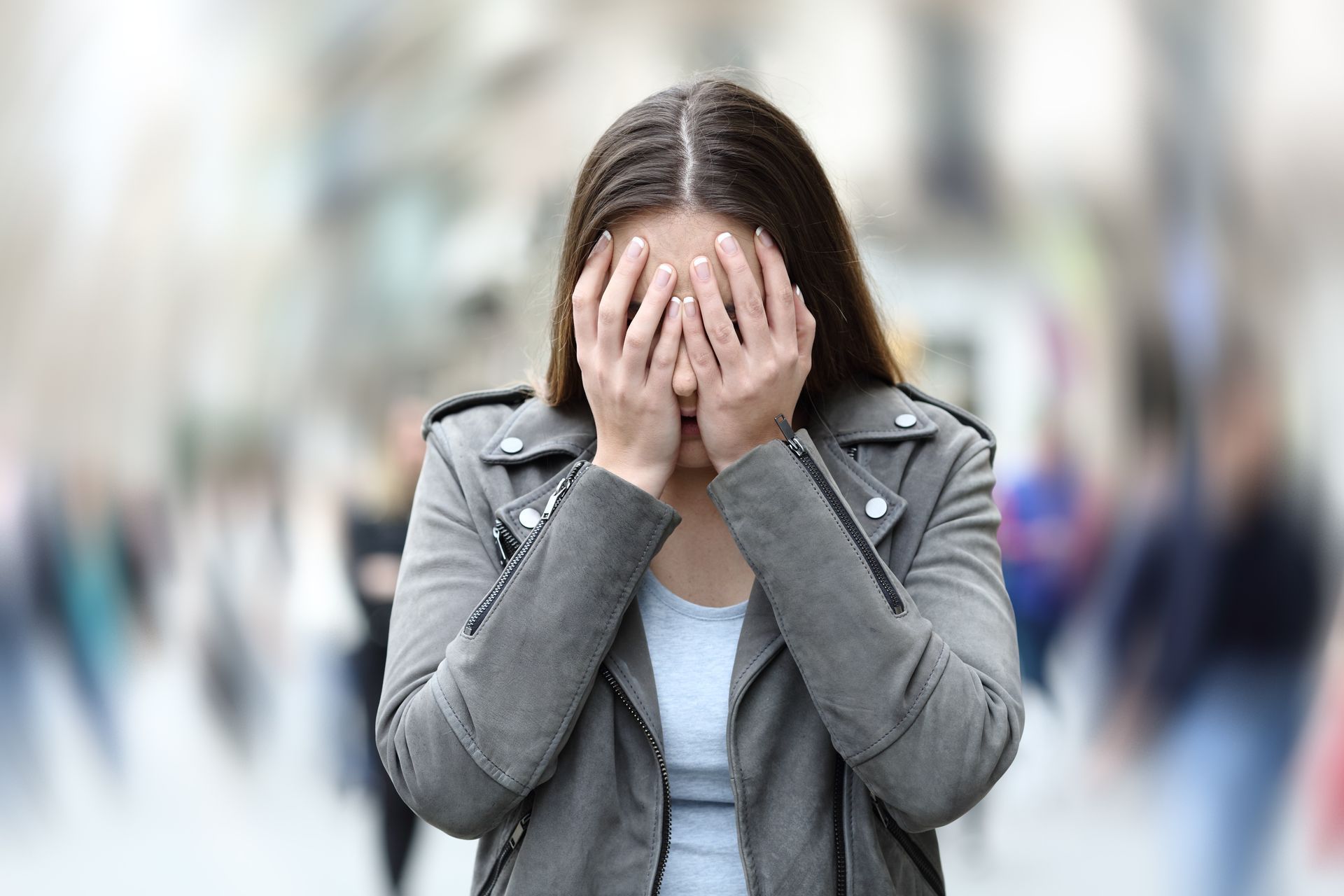 Une personne en veste se couvre le visage des deux mains dans une foule floue.