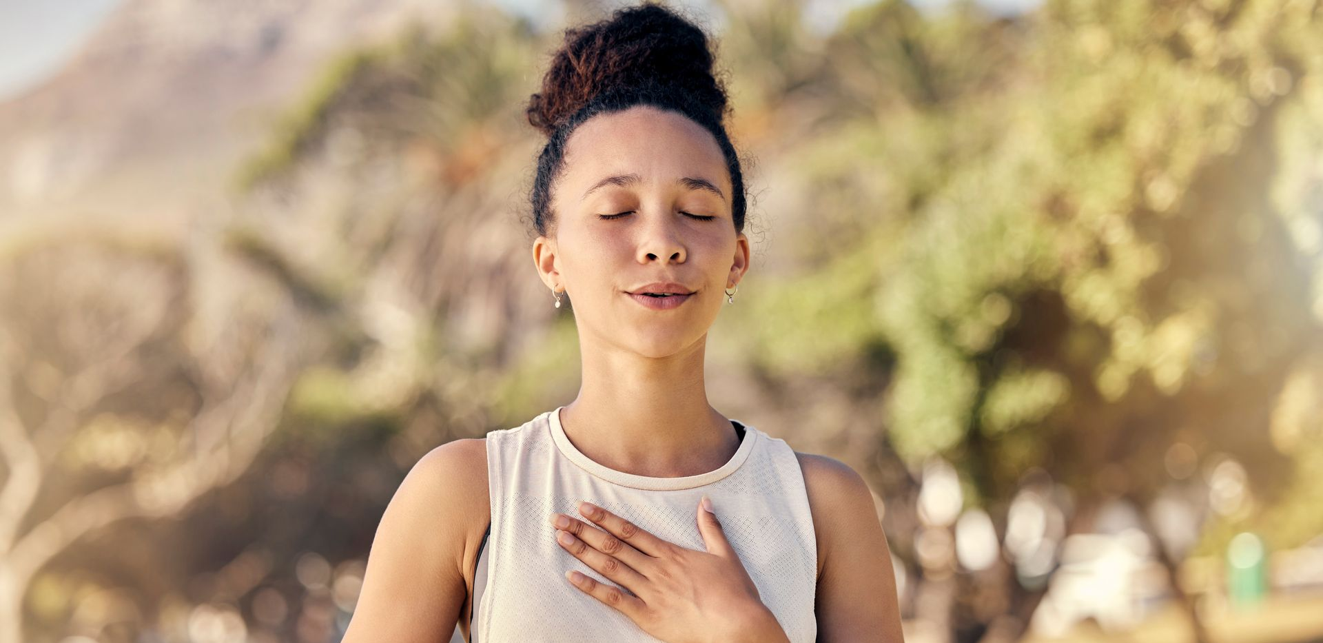 Personne méditant en plein air, les yeux fermés, la main sur la poitrine, dans un cadre naturel.