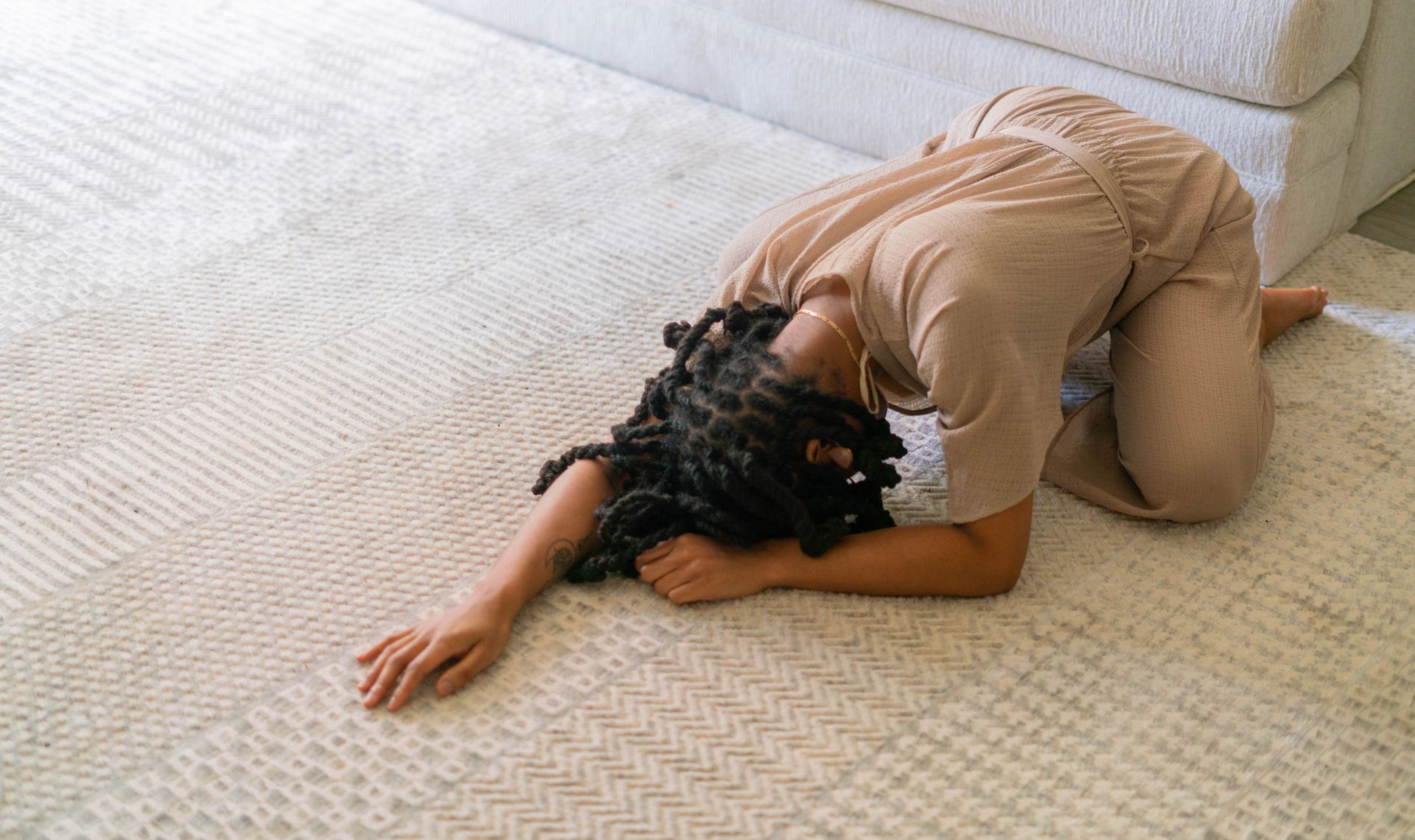 Une personne, vêtue d'une tenue, était recroquevillée face contre terre sur un tapis à côté d'un canapé.