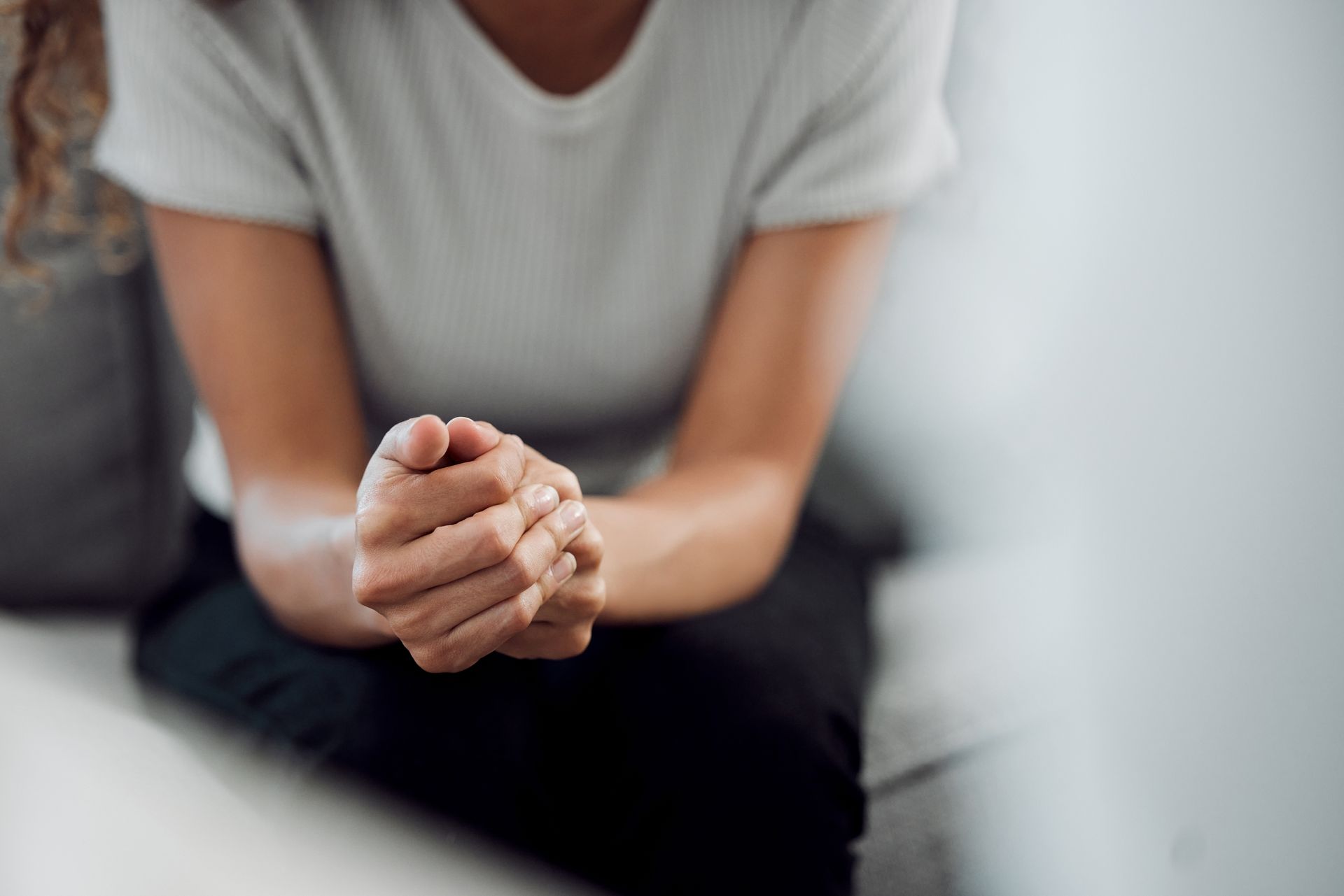 Une personne assise sur un canapé, les mains jointes, vêtue d'une chemise, dans une pièce.