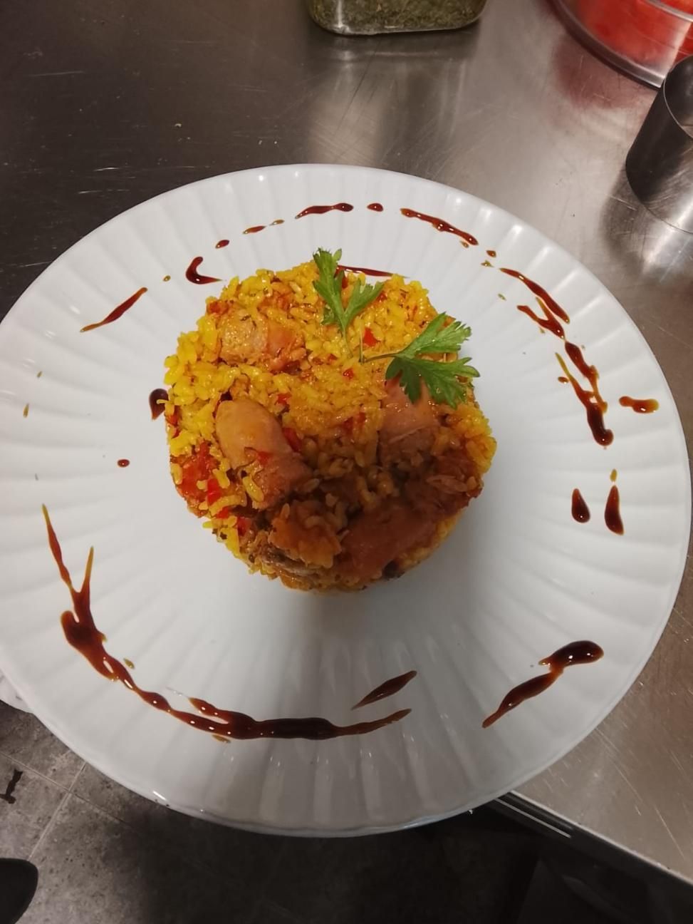 Plato de cuscús amarillo cubierto con carne, adornado con perejil y rociado con glaseado balsámico.