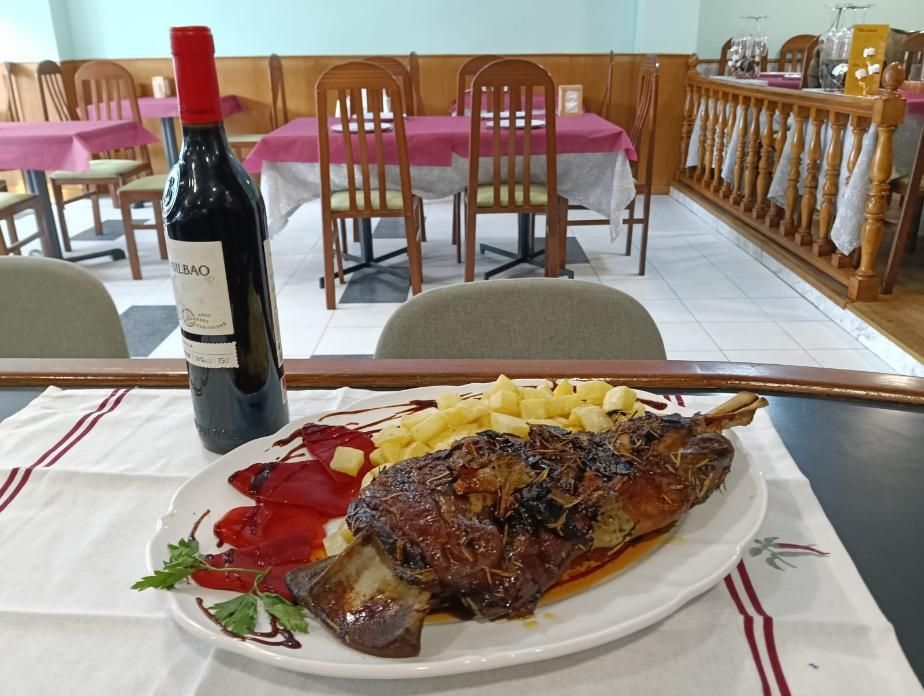 Carne asada y patatas en un plato con una botella de vino tinto sobre una mesa en un restaurante.