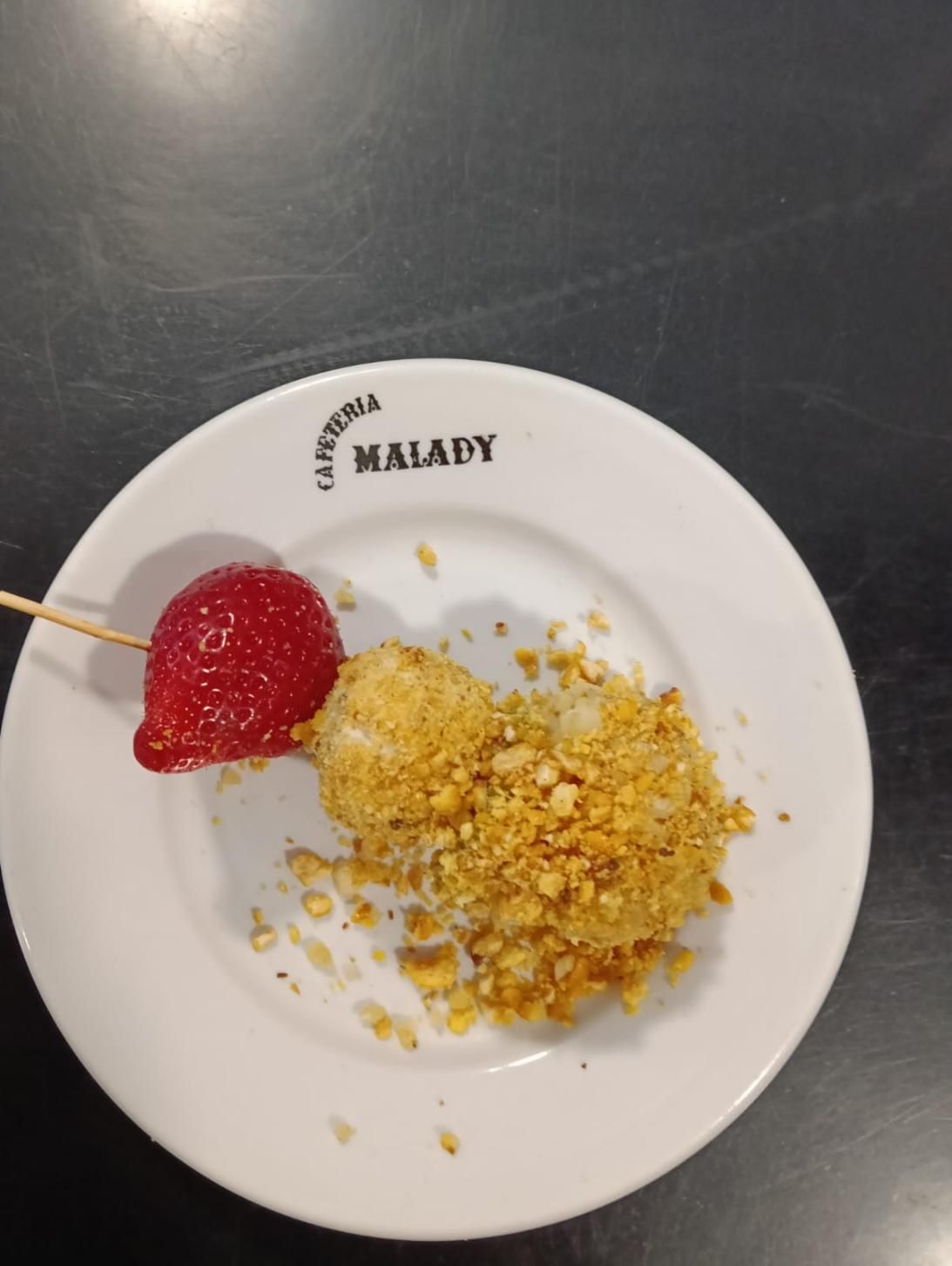 Caramelo de fresa en una brocheta, al lado de un postre rebozado en nueces trituradas