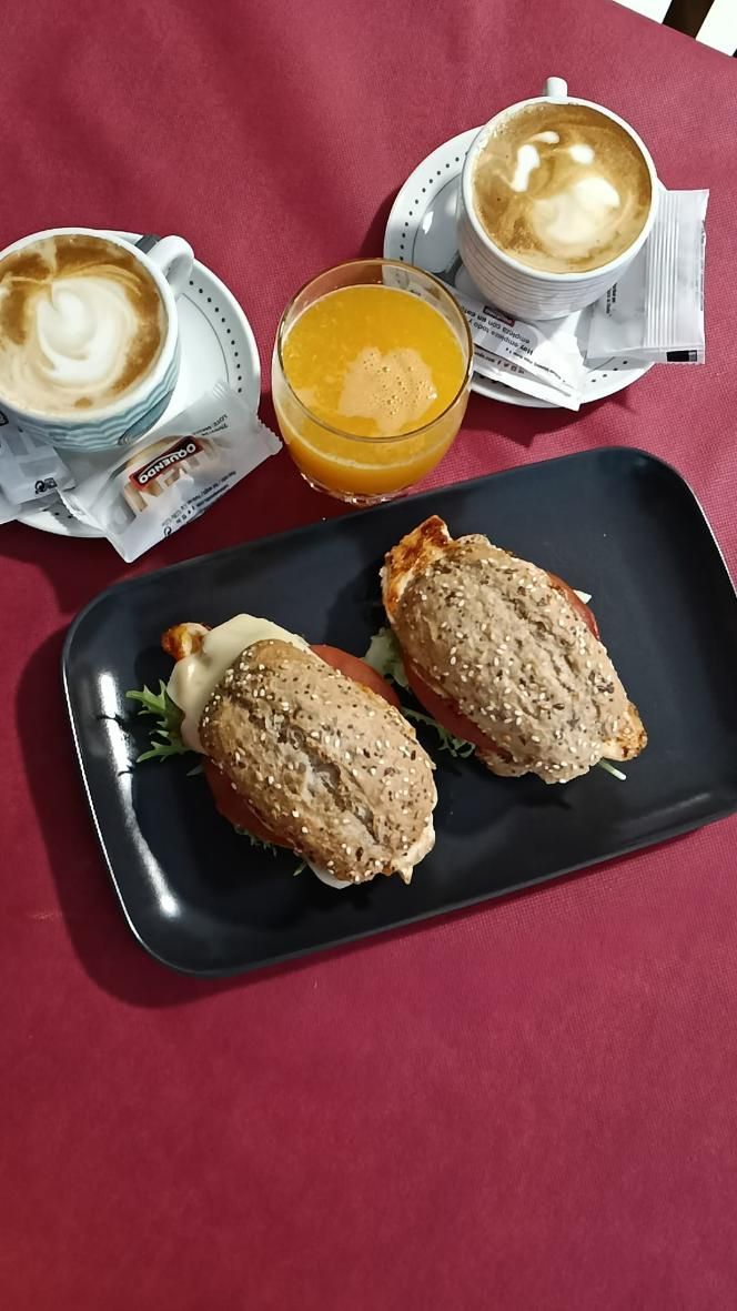 Sándwiches, café y jugo en una mesa. Dos tazas de capuchino, un vaso de jugo de naranja y un plato con dos sándwiches.