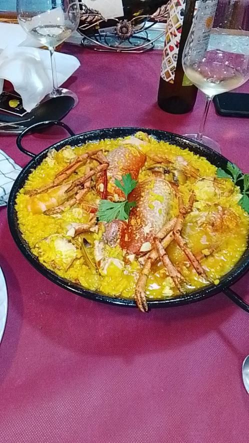 Paella en sartén negra con langosta encima, sobre una mesa roja.
