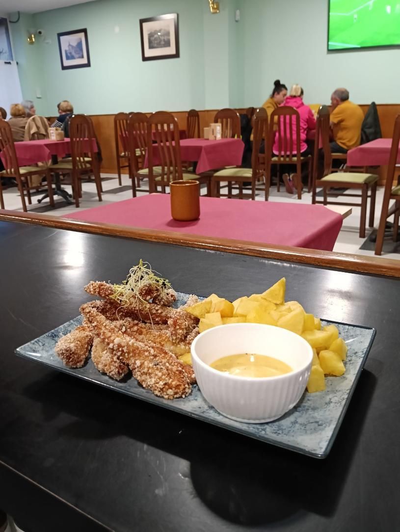 Tiras de pollo fritas, patatas y salsa para mojar en un plato en un restaurante.