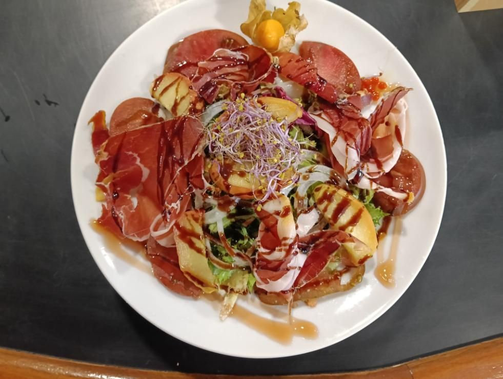 Plato de comida con carne cortada en rodajas, fruta y brotes, rociado con salsa.