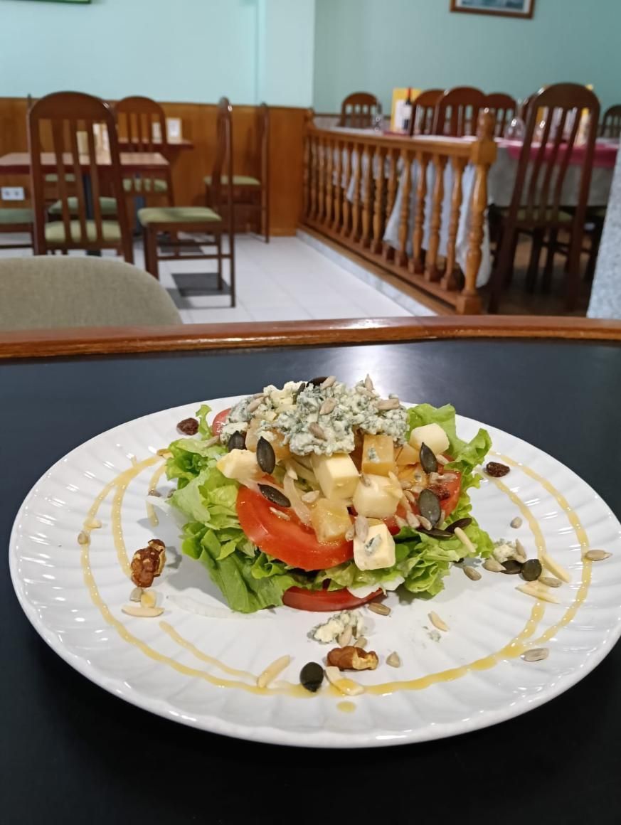 Ensalada con lechuga, tomate, queso y semillas, rociada con miel, en un plato blanco; en un comedor.