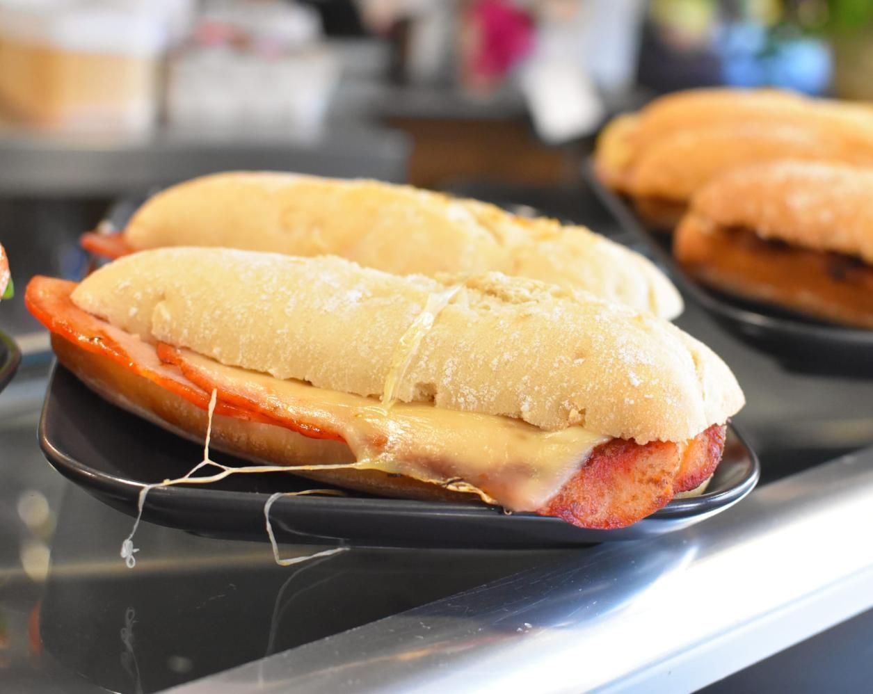 Sándwich en un plato oscuro, con queso fundido. Más sándwiches al fondo.
