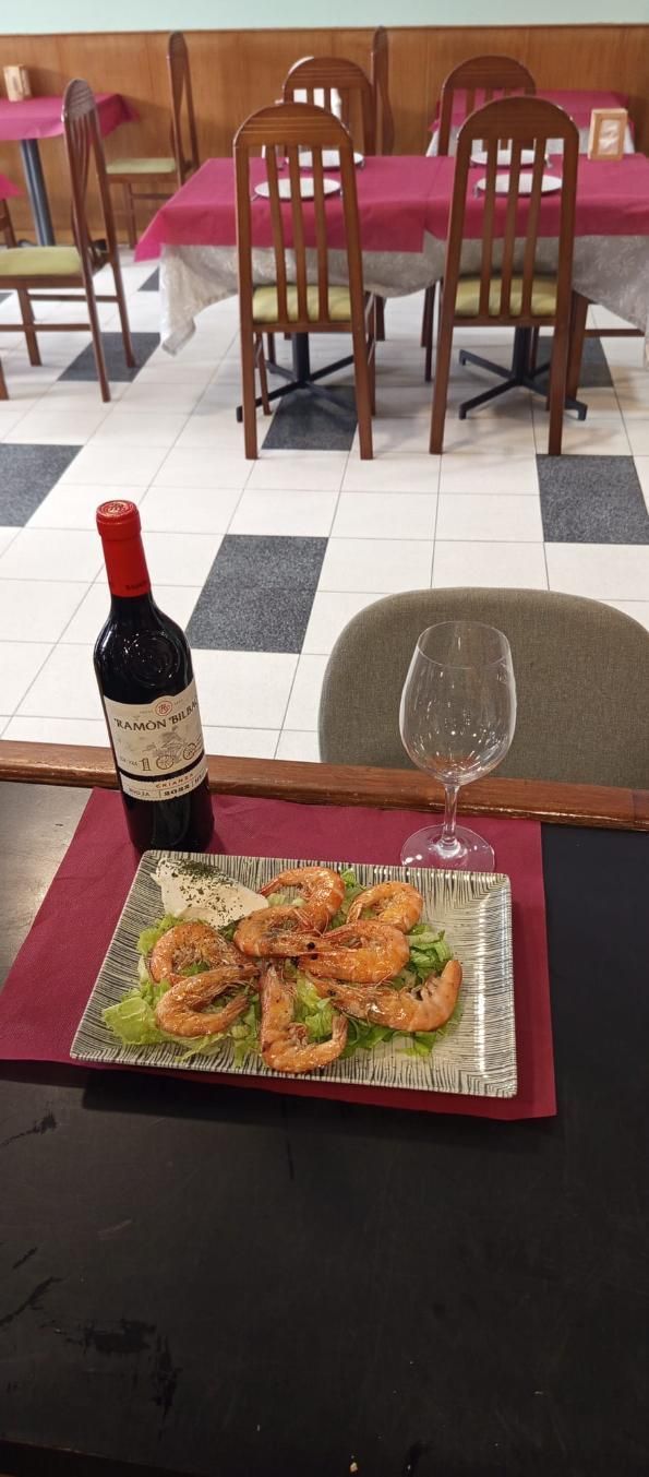 Plato de camarones, botella de vino y copa de vino sobre una mesa en un restaurante. Interior del comedor.