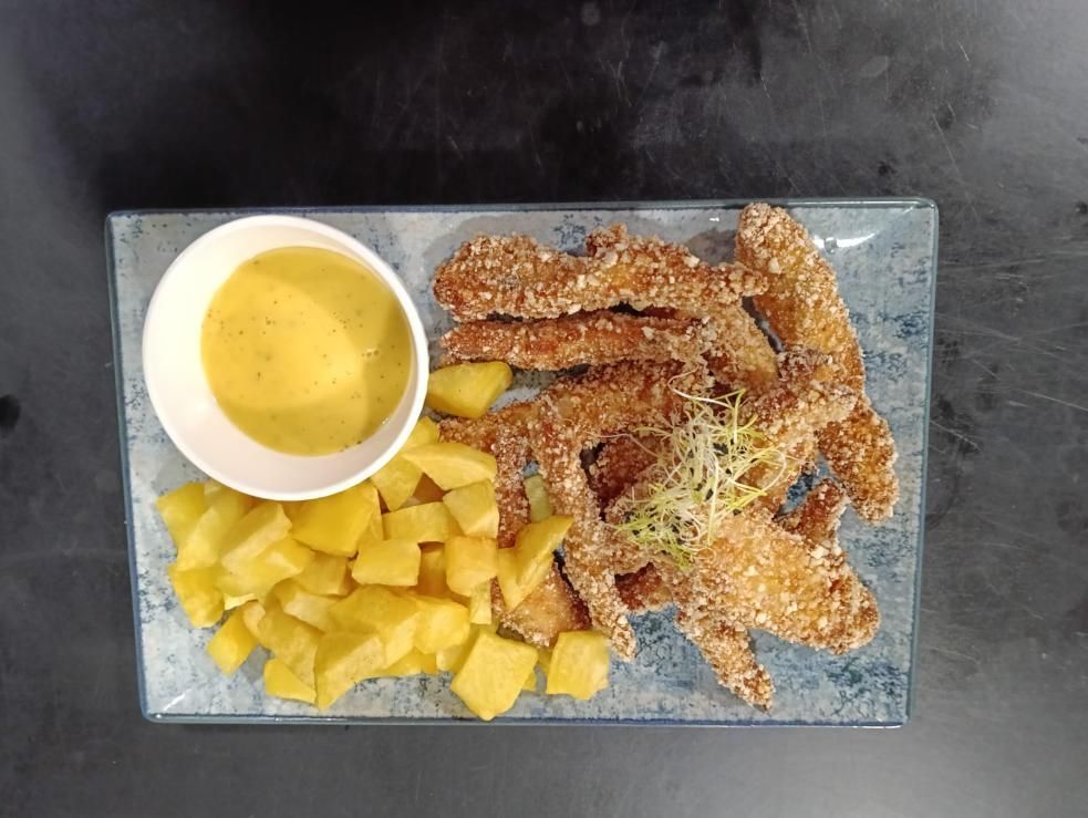 Plato de comida frita con salsa amarilla y patatas cortadas en cubitos.