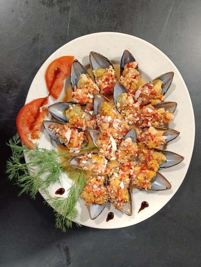 Plato de mejillones cocidos con topping, adornado con rodajas de tomate y eneldo.