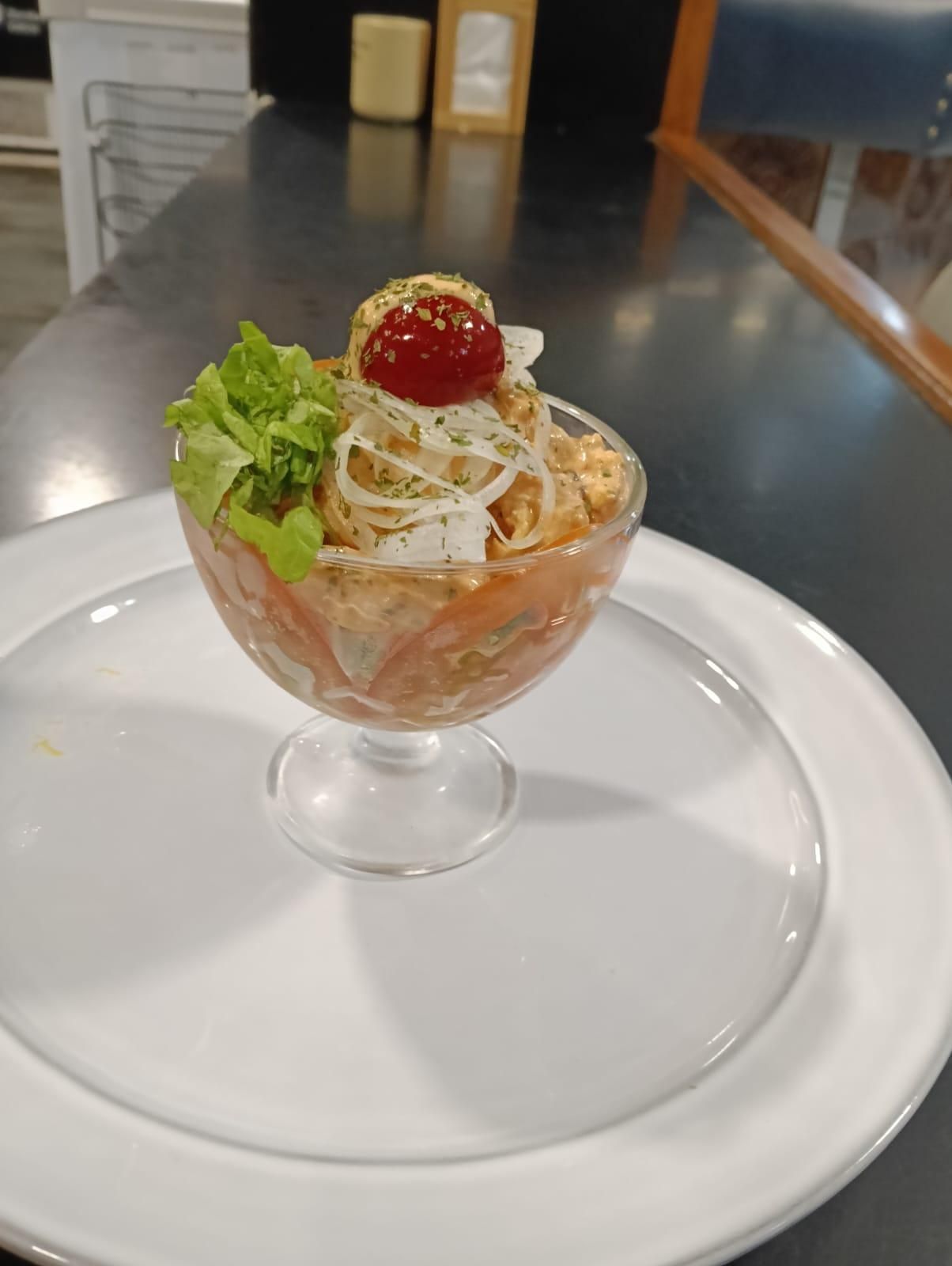 Un cóctel de camarones en vaso con lechuga, una cereza y plato blanco.