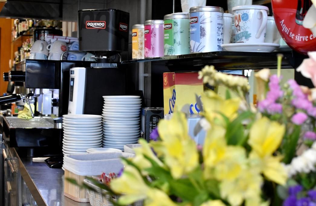 Mostrador de cafetería con platos apilados, máquina de café y arreglo floral.