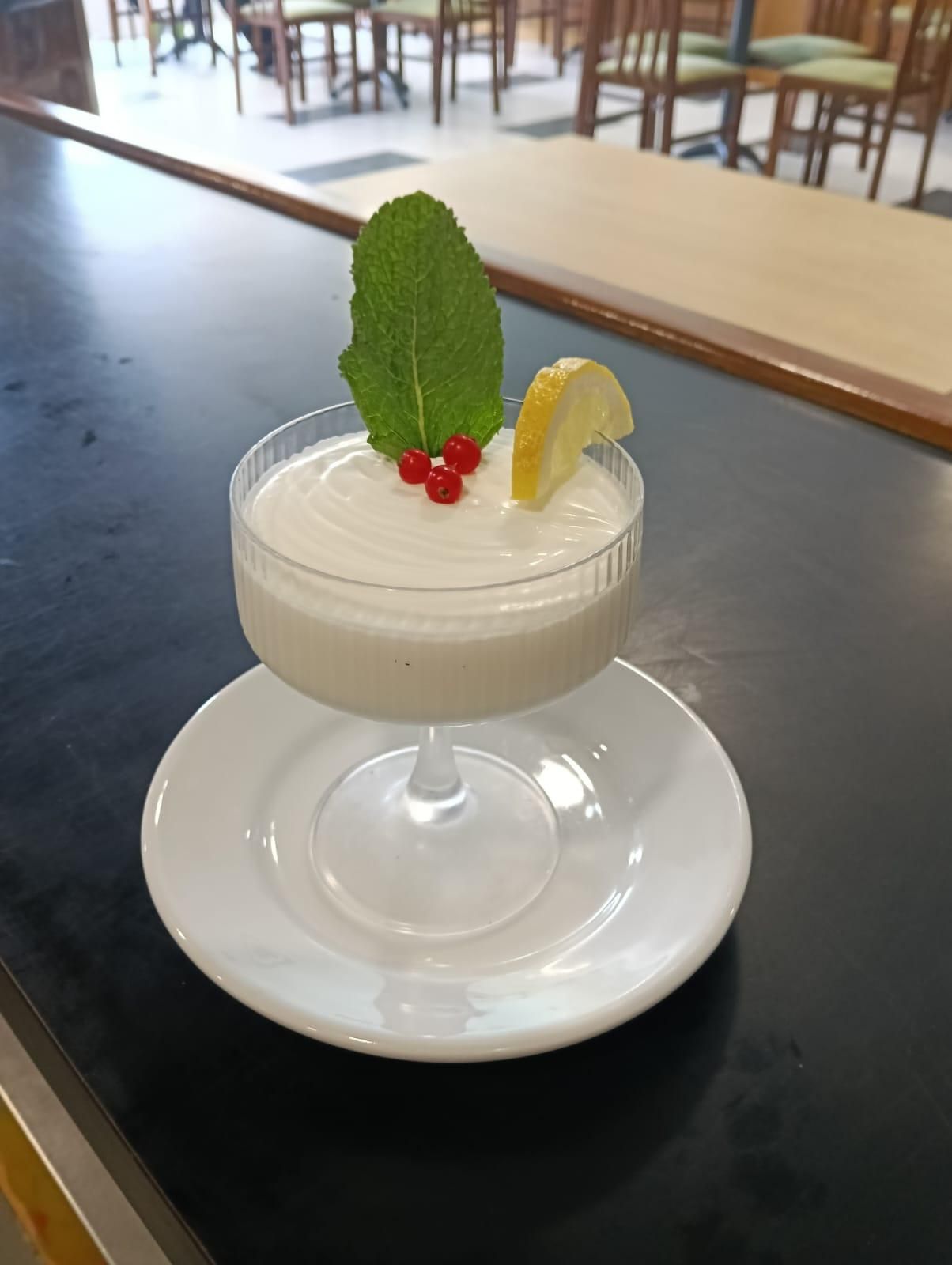 Postre de mousse blanca en copa, adornado con menta, bayas y limón, sobre un platillo.