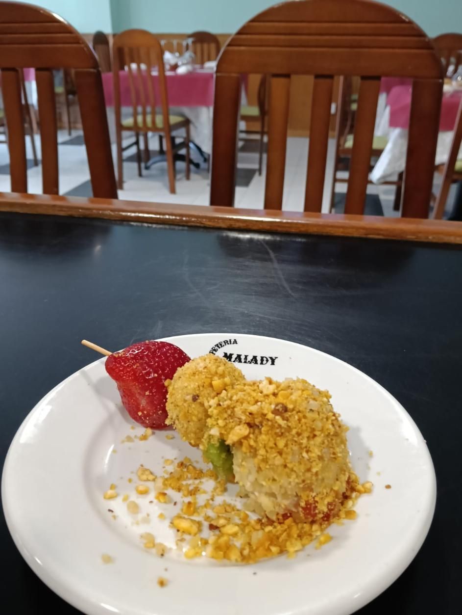 Postre en plato blanco: una bola frita, una rodaja de kiwi y una fresa. Ambiente de restaurante.