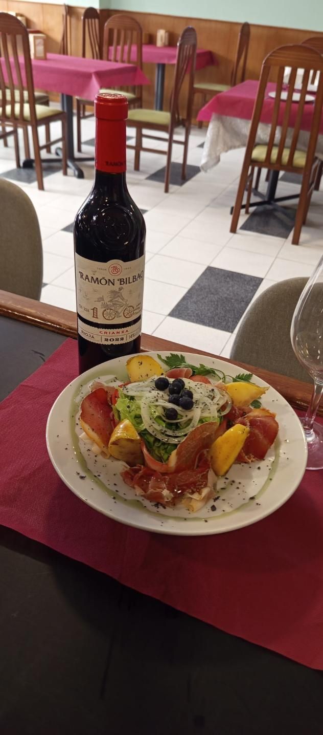 Una botella de vino tinto y un plato de comida en una mesa de un restaurante.