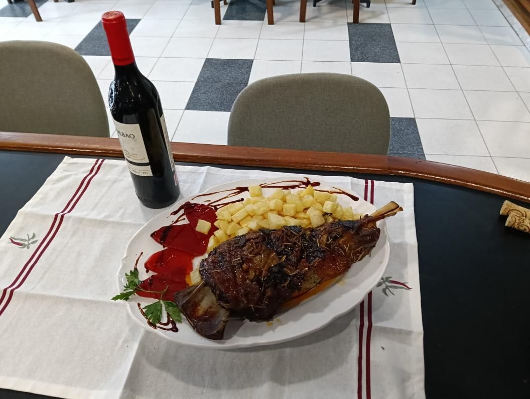 Plato de carne asada con patatas y botella de vino sobre una mesa.