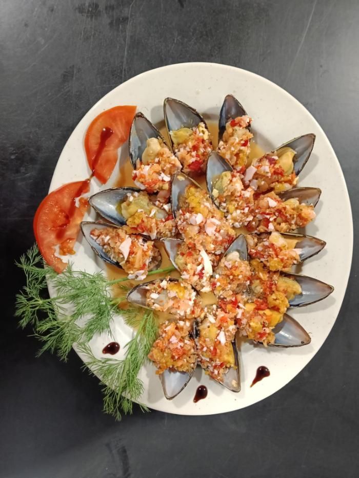 Plato de mejillones con topping, adornado con rodajas de tomate y eneldo.