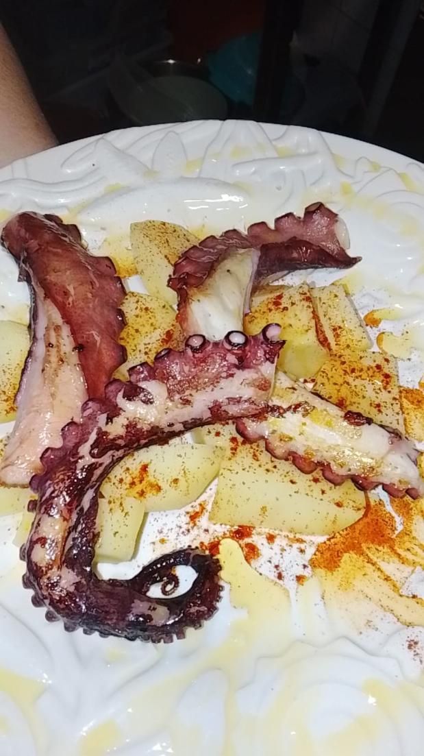 Pulpo en rodajas y patatas aliñadas con pimentón, sobre un plato blanco.