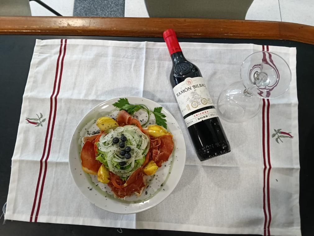 Un plato de comida, una botella de vino y una copa sobre un mantel blanco con rayas rojas.
