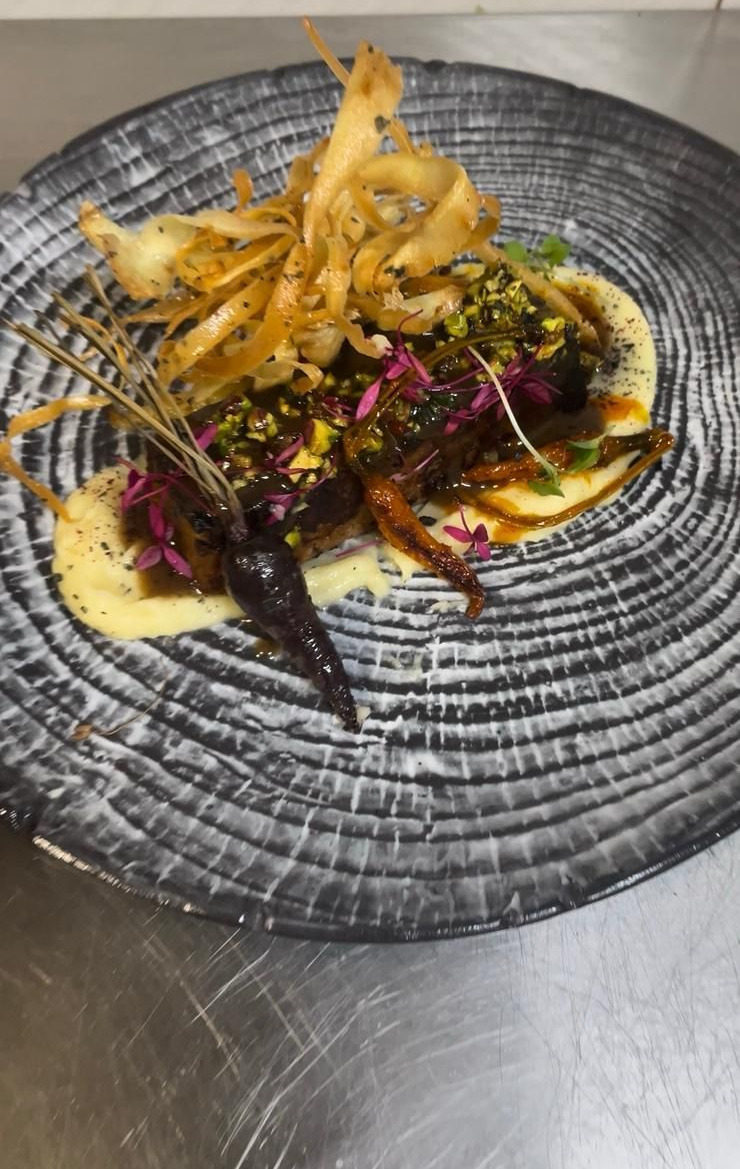 Un plato que incluye zanahorias moradas asadas, un corte de carne oscura