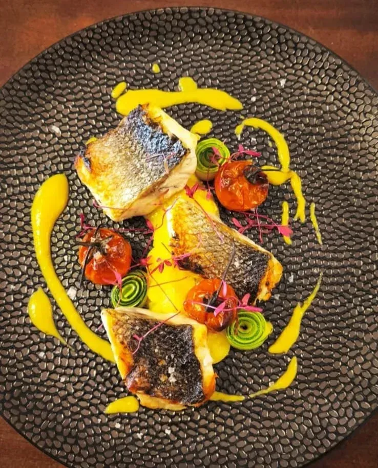 Tres filetes de pescado sellados, servidos con tomates asados, puerros en rodajas