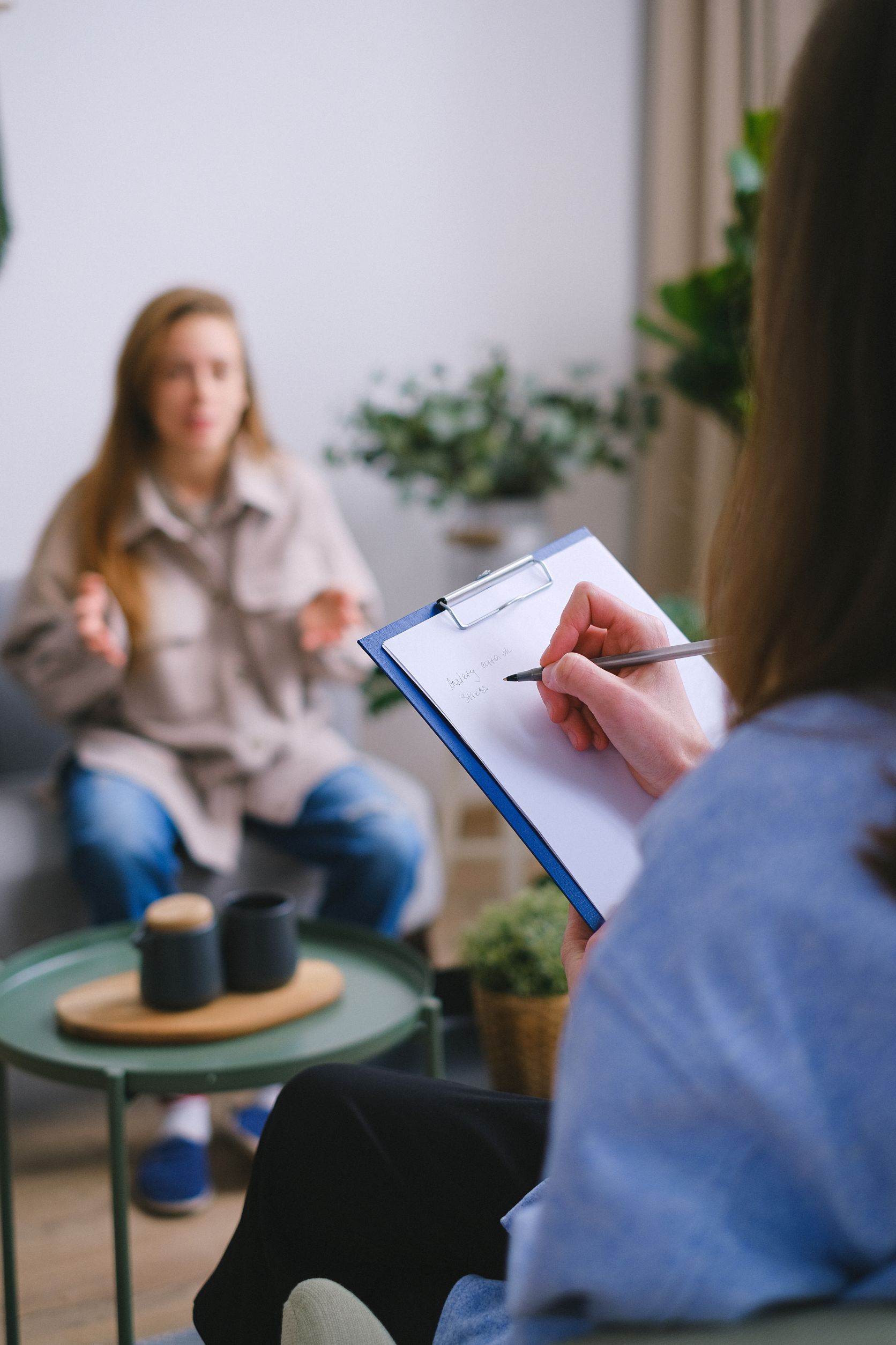 Una mujer está sentada en un sofá hablando con un terapeuta mientras sostiene un portapapeles.