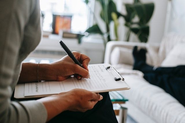 Una persona está sentada en un sofá escribiendo en un portapapeles.
