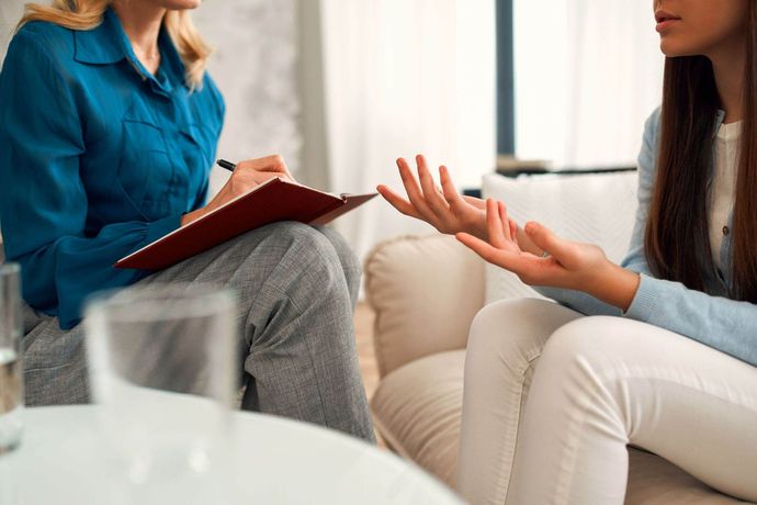 Una mujer está sentada en un sofá hablando con otra mujer.