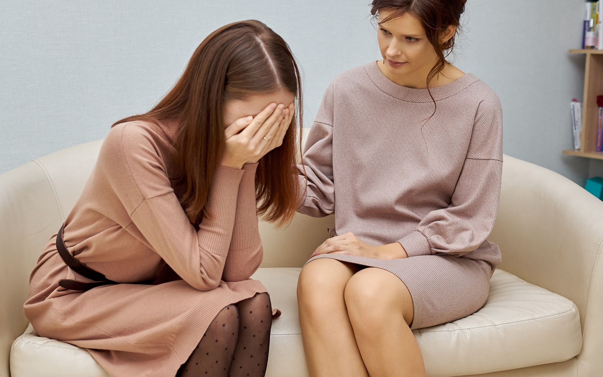 Una mujer está consolando a otra mujer que está llorando en un sofá.