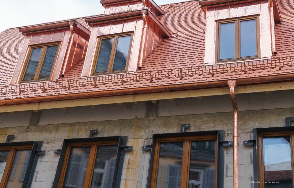 Kupferdach mit drei Dachgauben und Kupferrinnen an einem Gebäude mit Steinfassade.