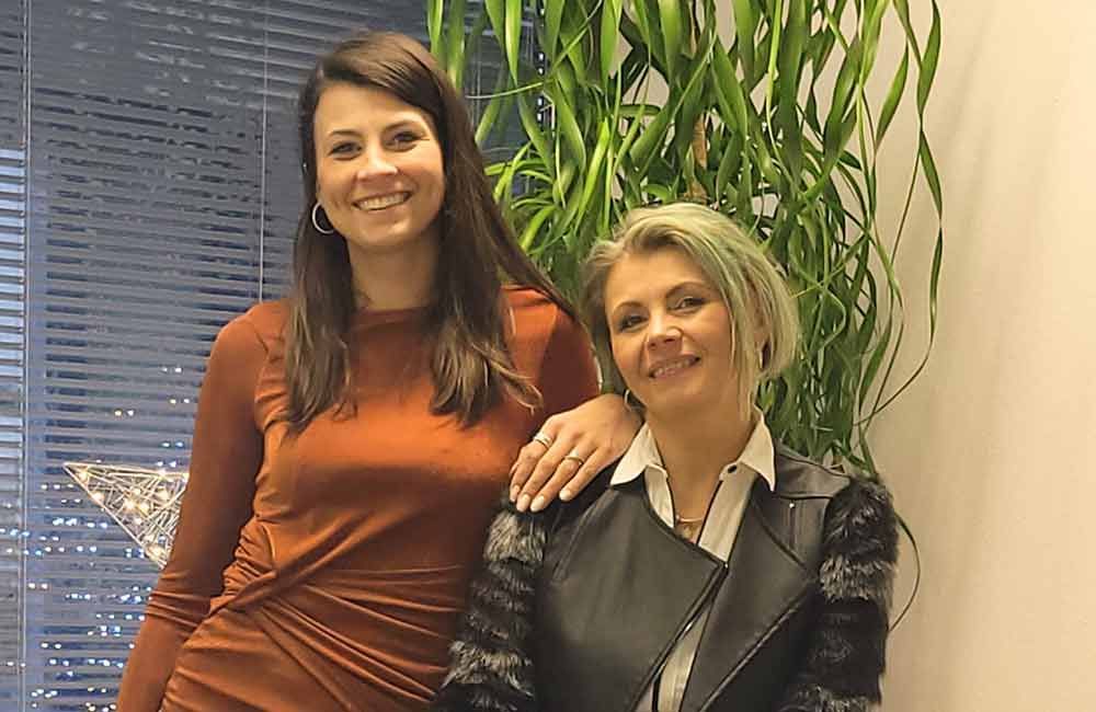 Zwei Frauen posieren vor einer Pflanze für ein Foto.