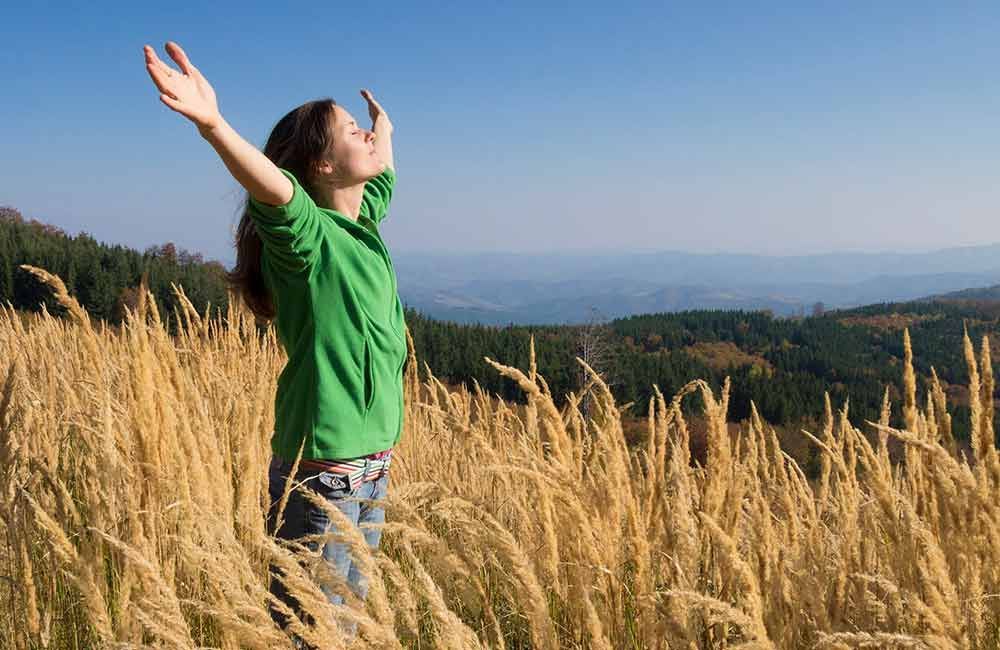 Eine Frau in einem grünen Hemd steht mit ausgestreckten Armen auf einem Feld.