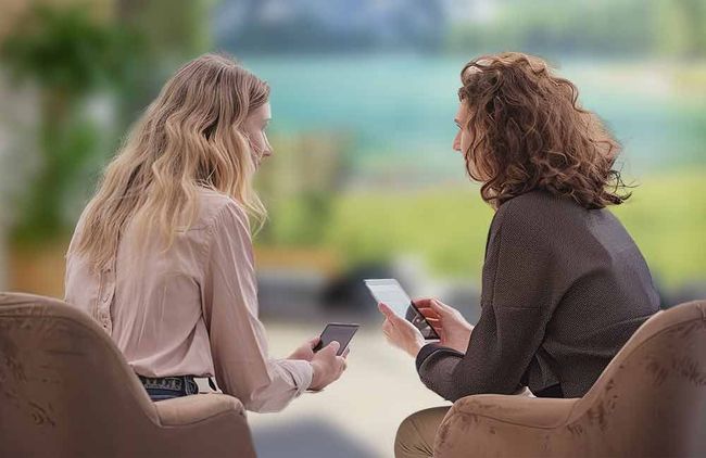 Zwei Frauen sitzen auf Stühlen und schauen auf ihre Handys.