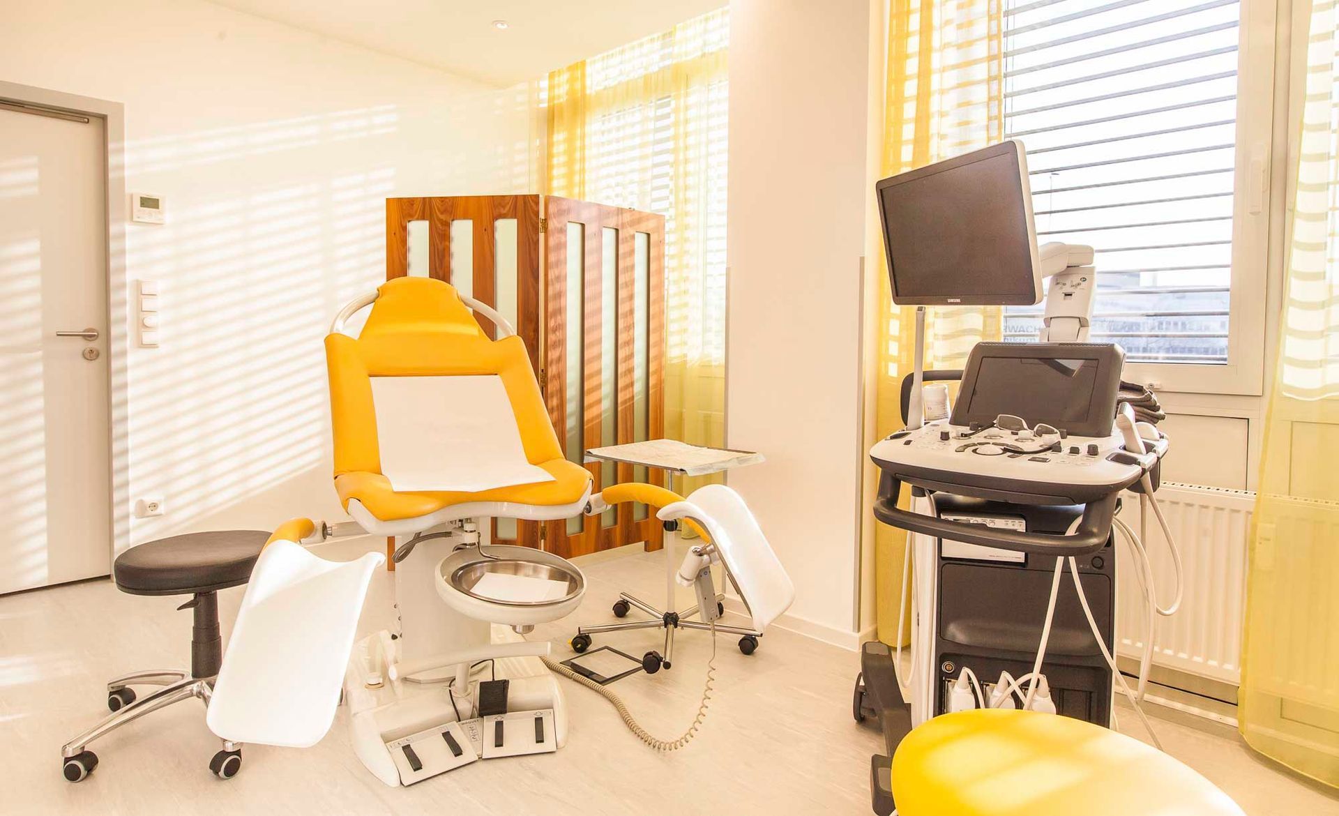 Eine Arztpraxis mit Stuhl, Hocker und Ultraschallgerät.