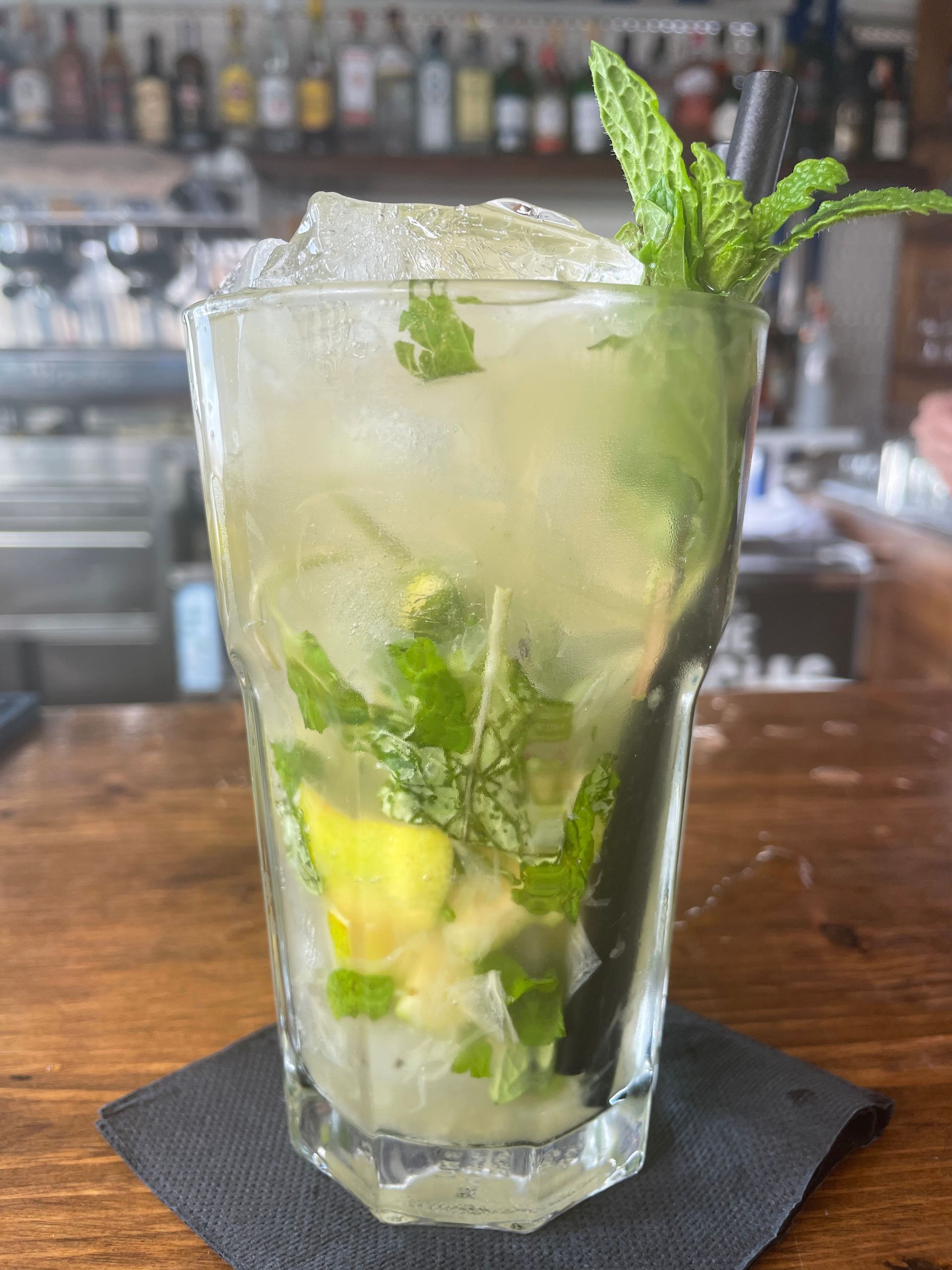 Un vaso de mojito está sobre una servilleta en una barra.