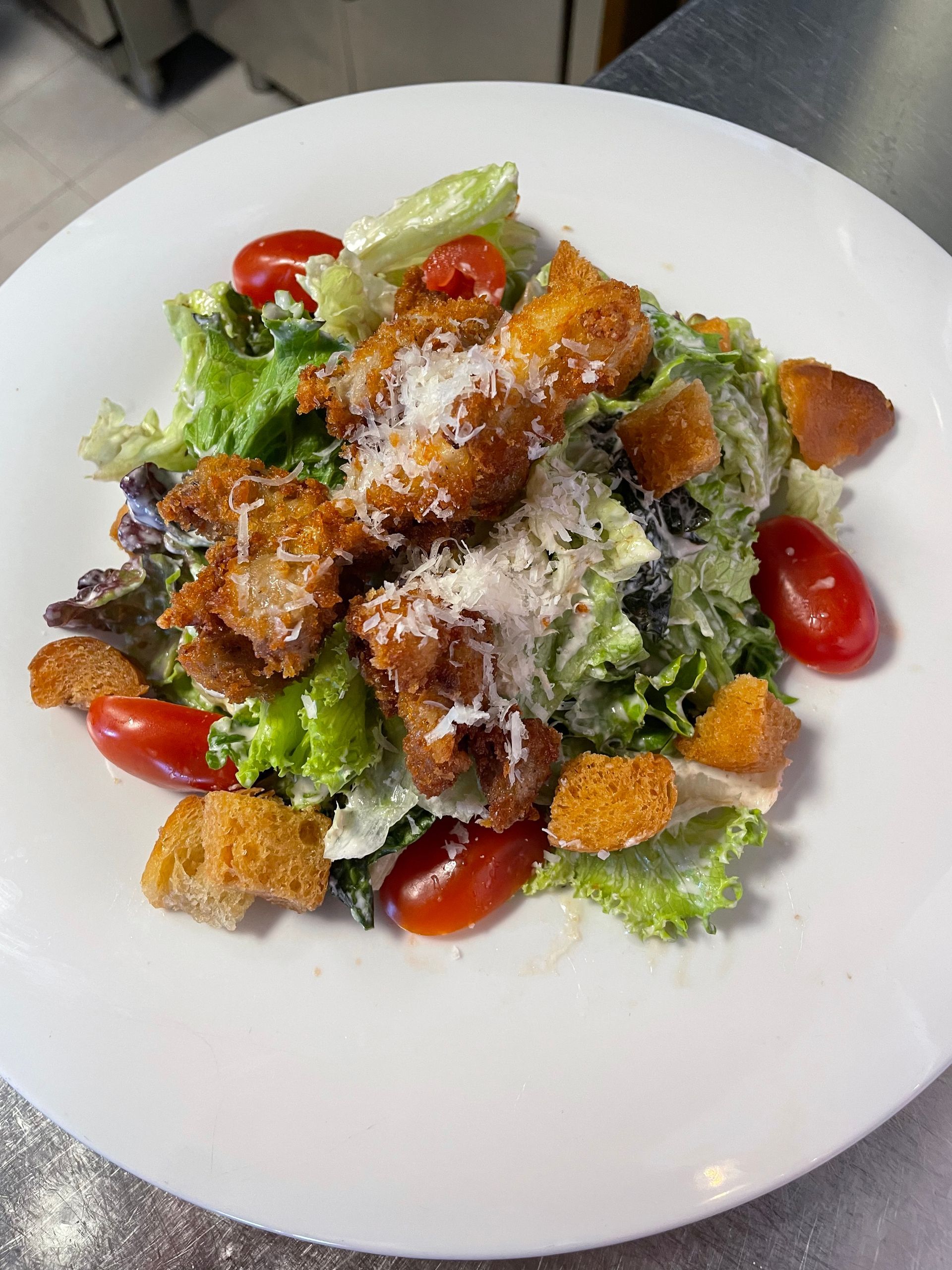 Una ensalada con pollo, lechuga, tomates y crutones en un plato blanco.