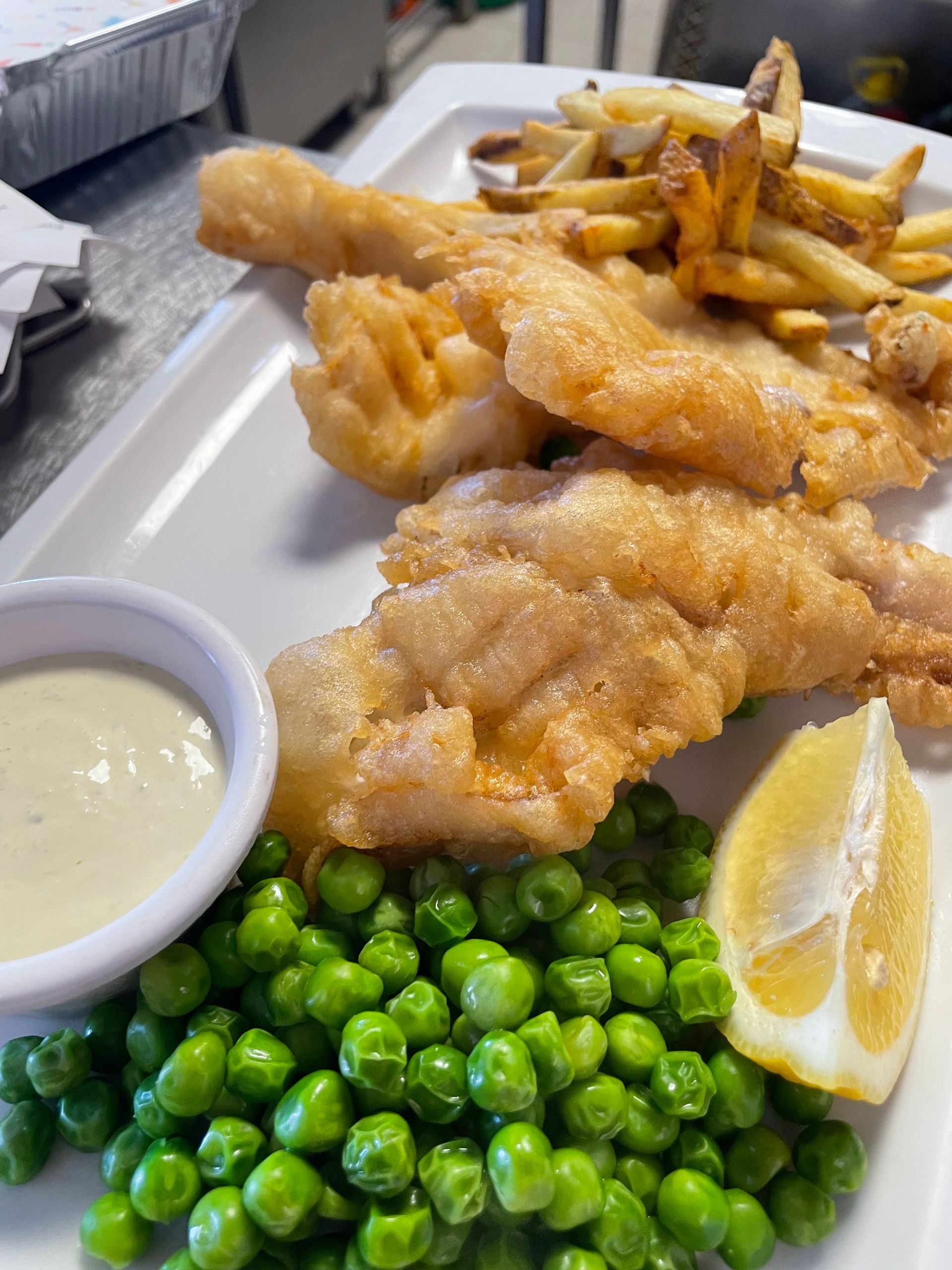 Un plato de pescado y patatas fritas con guisantes y una rodaja de limón sobre una mesa.