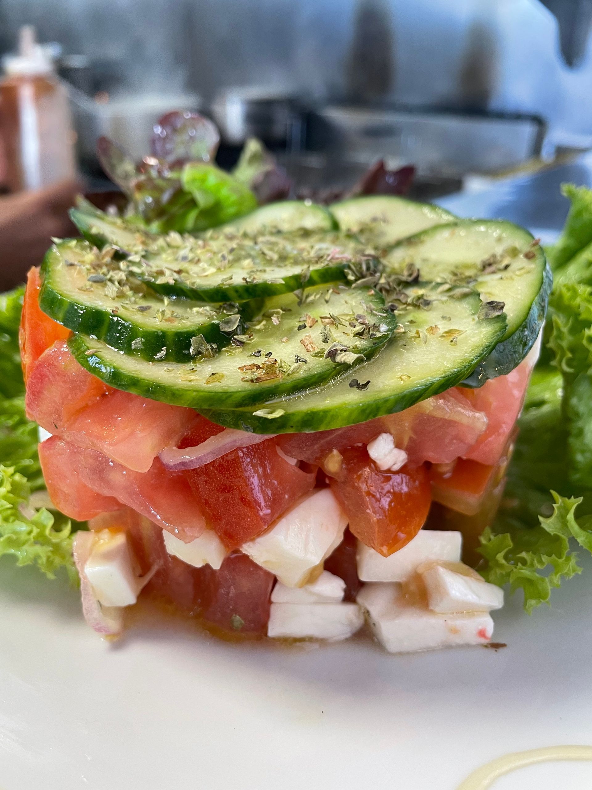 Una ensalada con tomates, pepinos, queso y lechuga en un plato blanco.