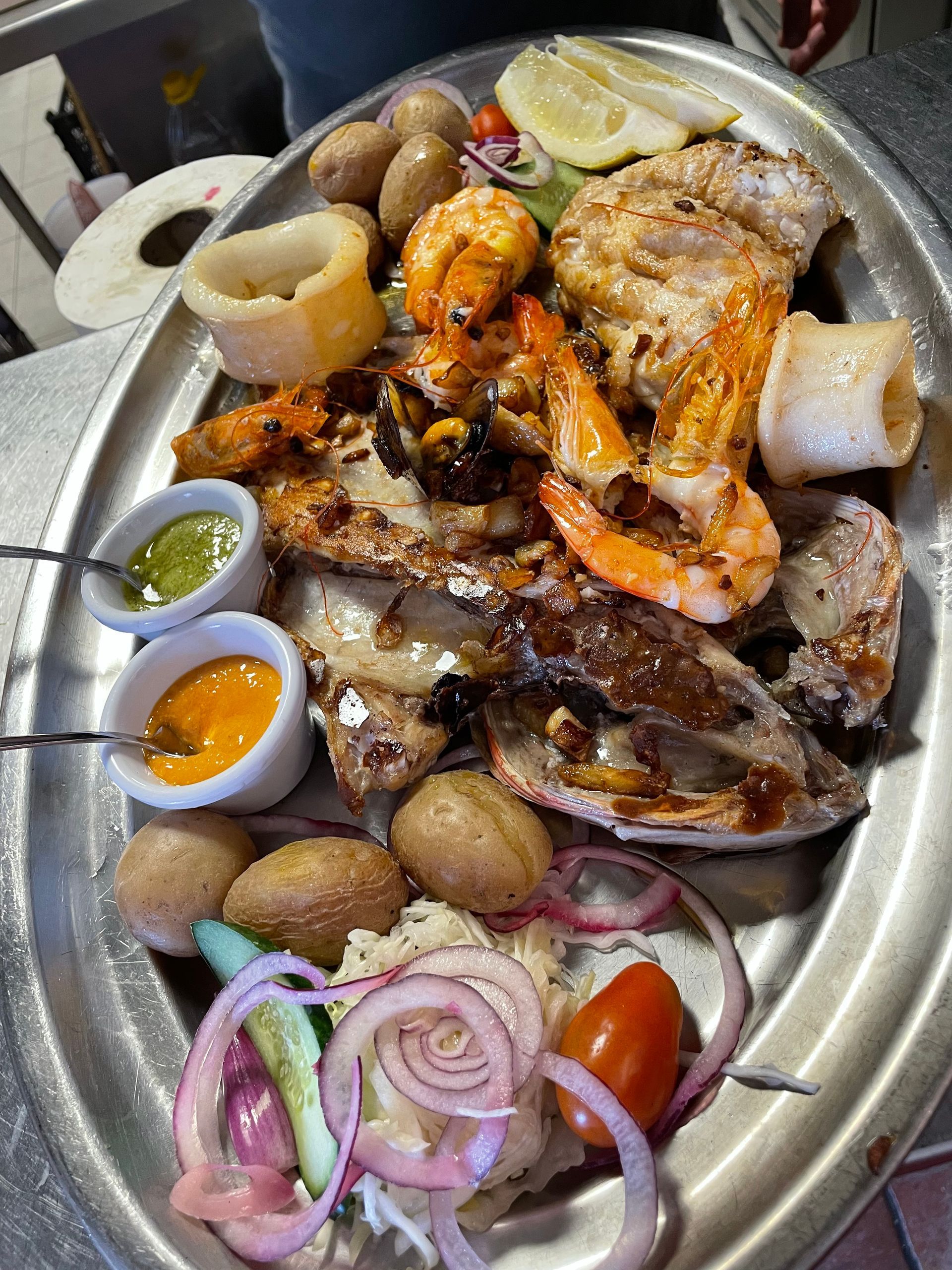 Un plato de comida con carne, camarones, papas, cebollas y salsas en una mesa.