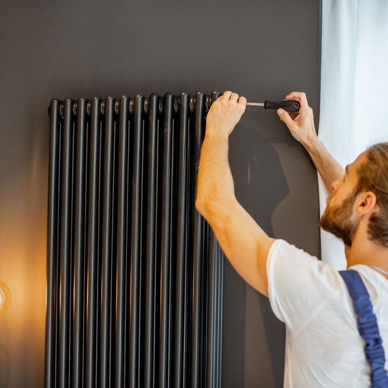 Un hombre está arreglando un radiador con un destornillador.