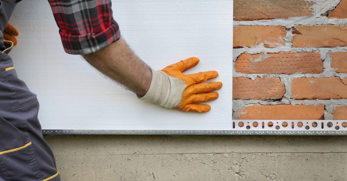 Un hombre sostiene un trozo de poliestireno junto a una pared de ladrillos.