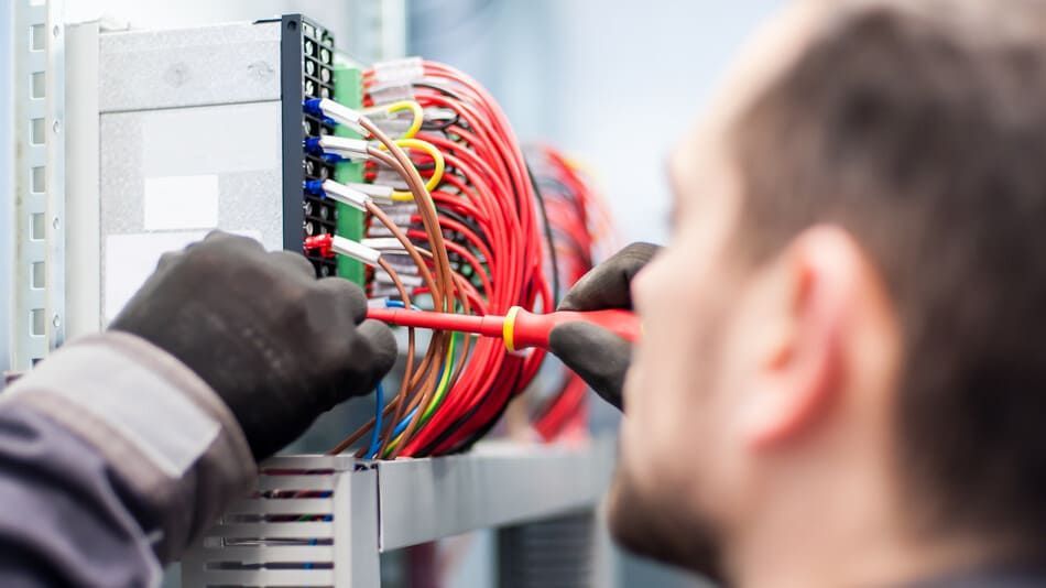 Un hombre está trabajando en una caja eléctrica con un destornillador.