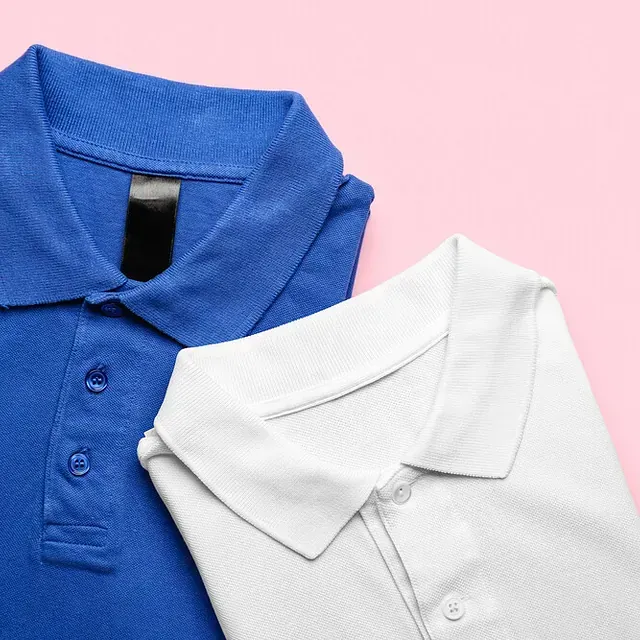 Un polo azul y un polo blanco están doblados sobre una superficie rosa.