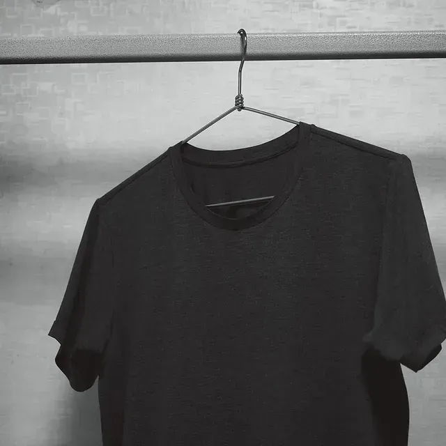 Una camiseta negra está colgada en una percha en un armario.