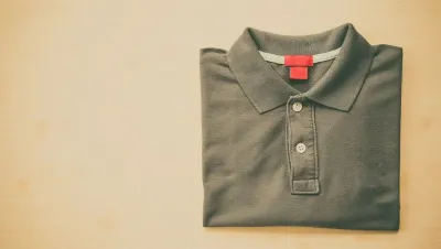 Un polo doblado con cuello rojo está sobre una mesa de madera.